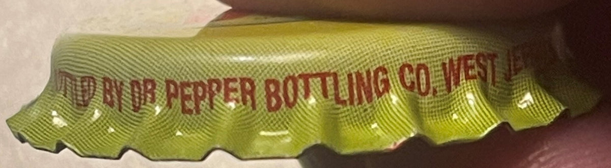 Yellow-green vintage bottle cap with red embossed text reading "Dr Pepper Bottling Co West" shown at angle against brown back