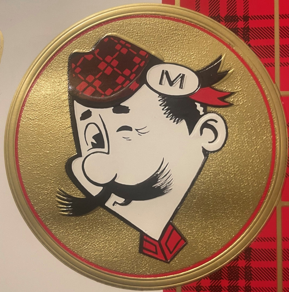 Circular embossed cigar box label featuring a caricatured Scottish man wearing a red tartan tam o'shanter hat with "M" on a s