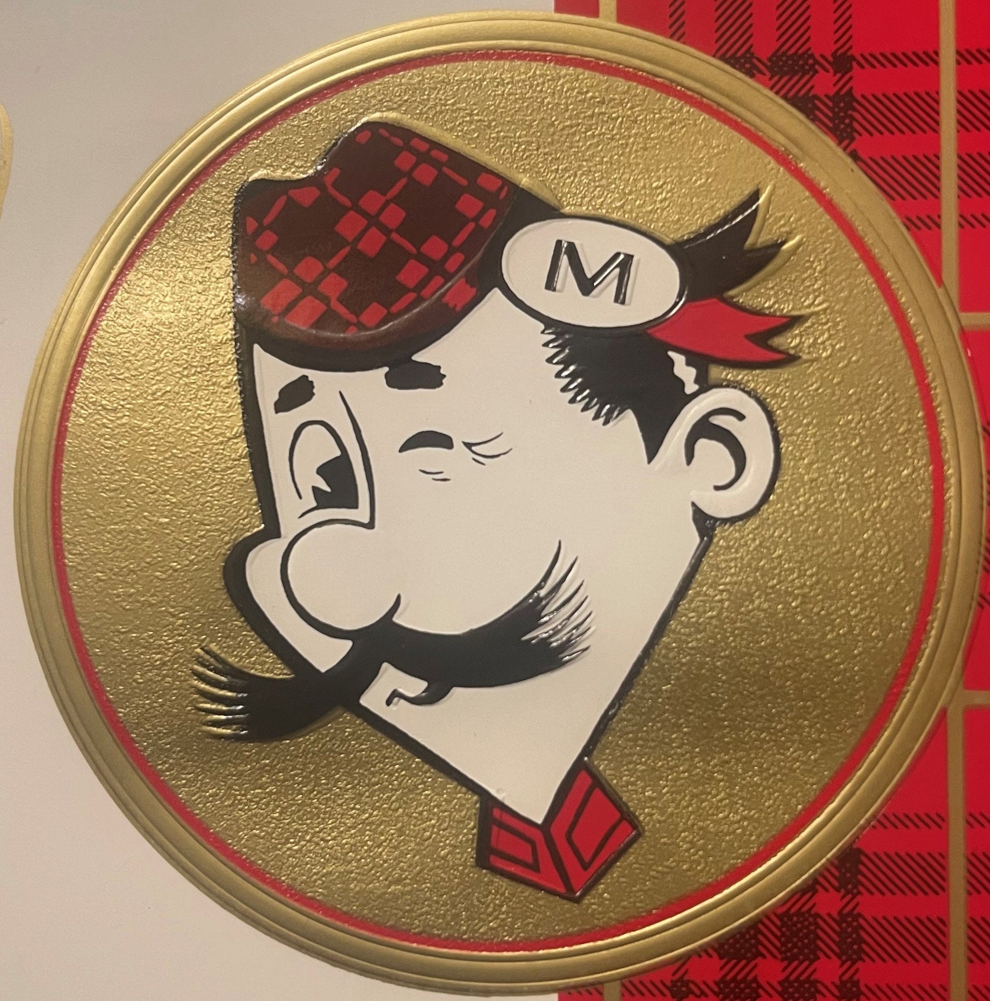 Circular embossed cigar box label featuring a caricatured Scottish man wearing a red tartan tam o'shanter hat with "M" on a s