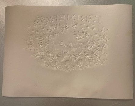 Cream-colored embossed cigar label with ornate scrollwork border and central steamship design, photographed flat against neut