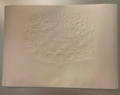 Cream-colored embossed cigar label with ornate scrollwork border and central steamship design, photographed flat against neut