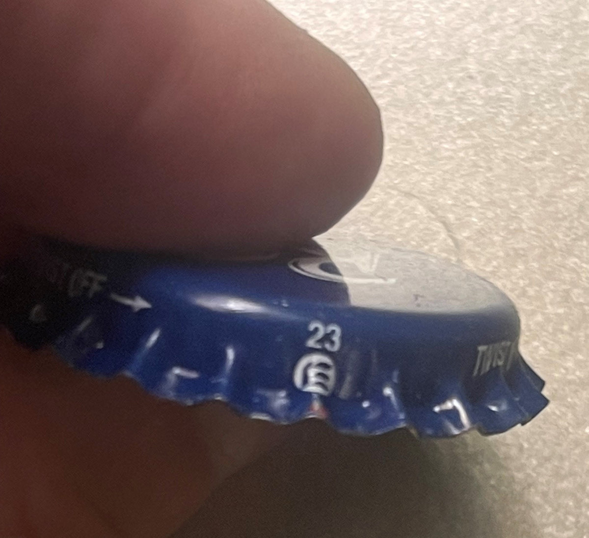 Blue metal bottle cap held in hand showing "23" and "Dr Pepper" text, close-up detail view