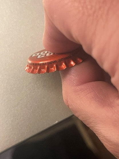 Red Double Cola bottle cap held between fingers showing ridged crown and printed text, close-up detail shot