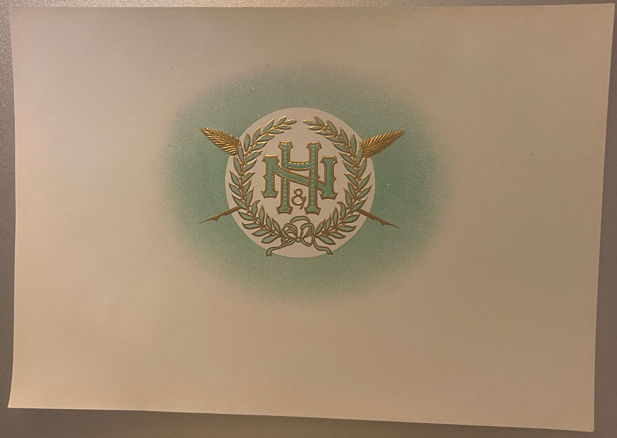N&H embossed cigar label on cream paper: the gold and green N&H monogram in a laurel wreath with crossed feathered shafts and a ribbon bow, centered in a soft green halo