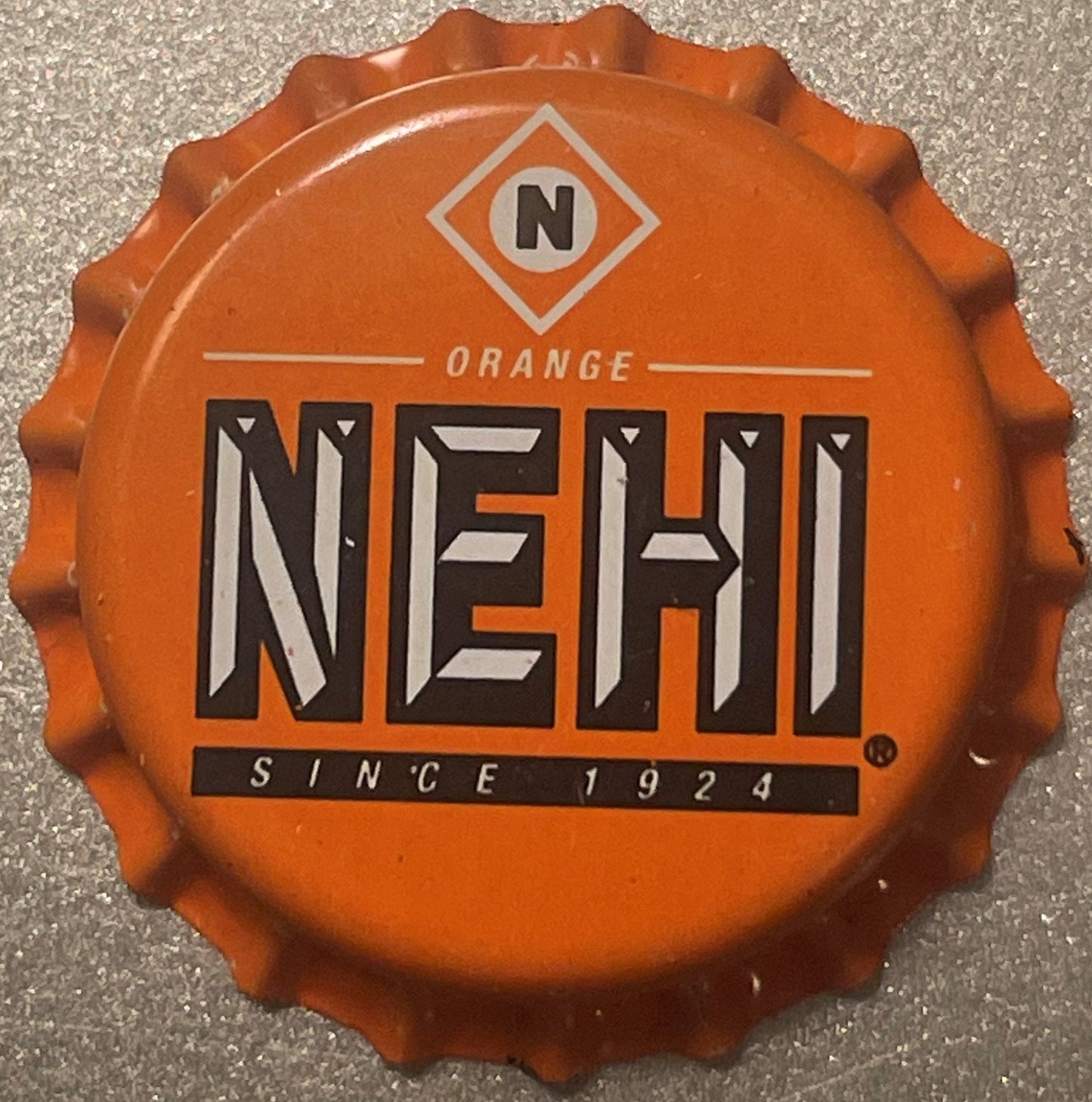 Orange Nehi bottle cap with ridged edges, displaying "N" diamond logo, "ORANGE" text, large "NEHI" lettering, and "SINCE 1924