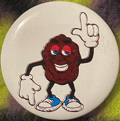 Vintage California Raisin tin pin featuring brown raisin character with red eyes, white smile, blue sneakers, pointing upward