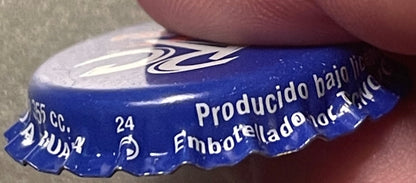 Close-up of blue Royal Crown Cola bottle cap held by a thumb, showing white wavy logo and embossed