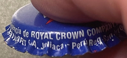 Close-up of blue Royal Crown Cola bottle cap held by a hand, showing embossed text and red accent detail.