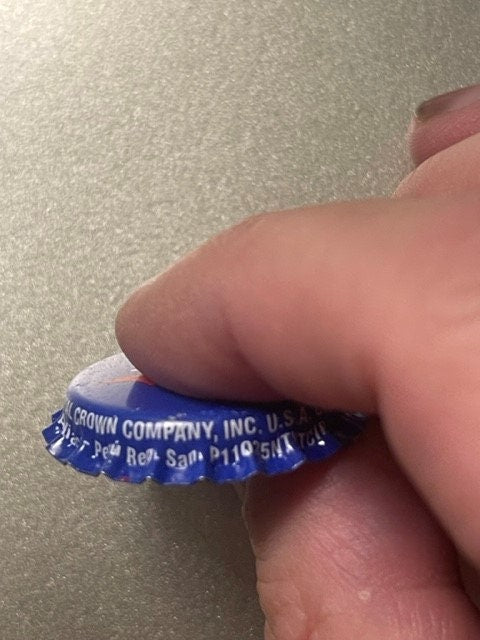 Vintage blue Royal Crown Cola bottle cap held in fingers for scale, showing embossed text and crown logo detail