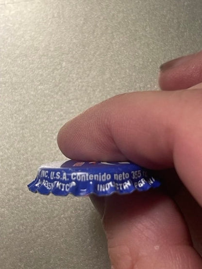 Close-up of blue bottle cap held by human finger showing embossed text including "U.S.A."