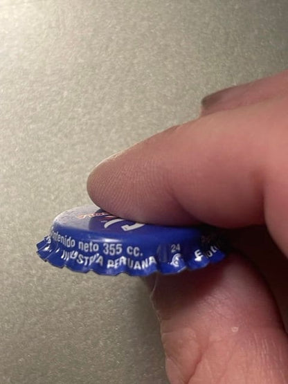 Close-up of blue RC Cola bottle cap held between fingertip and thumb, showing embossed text and ridged crown edge details.