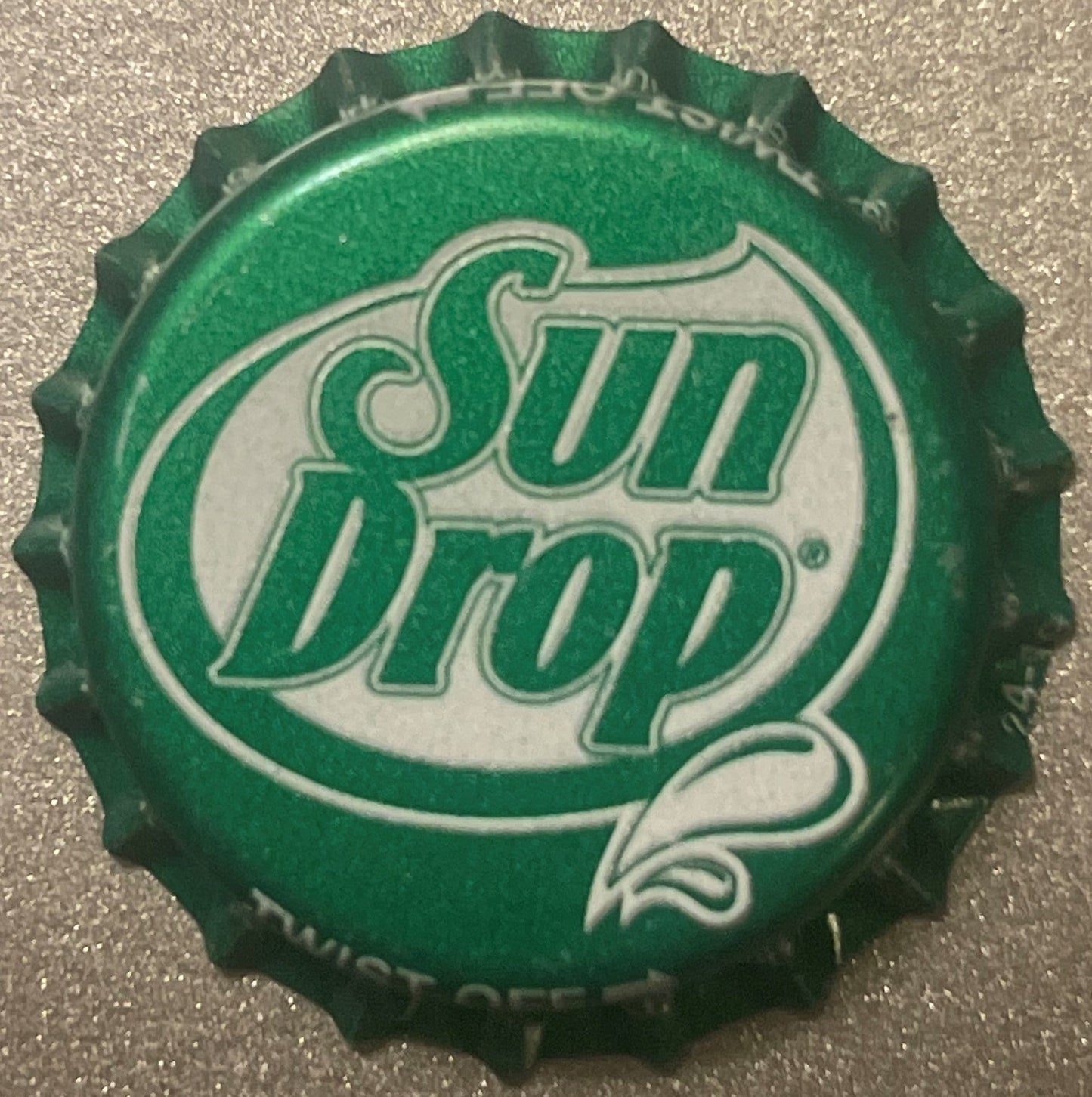 Green and white twist-off bottle cap with "Sun Drop" logo on textured background, shown flat from above