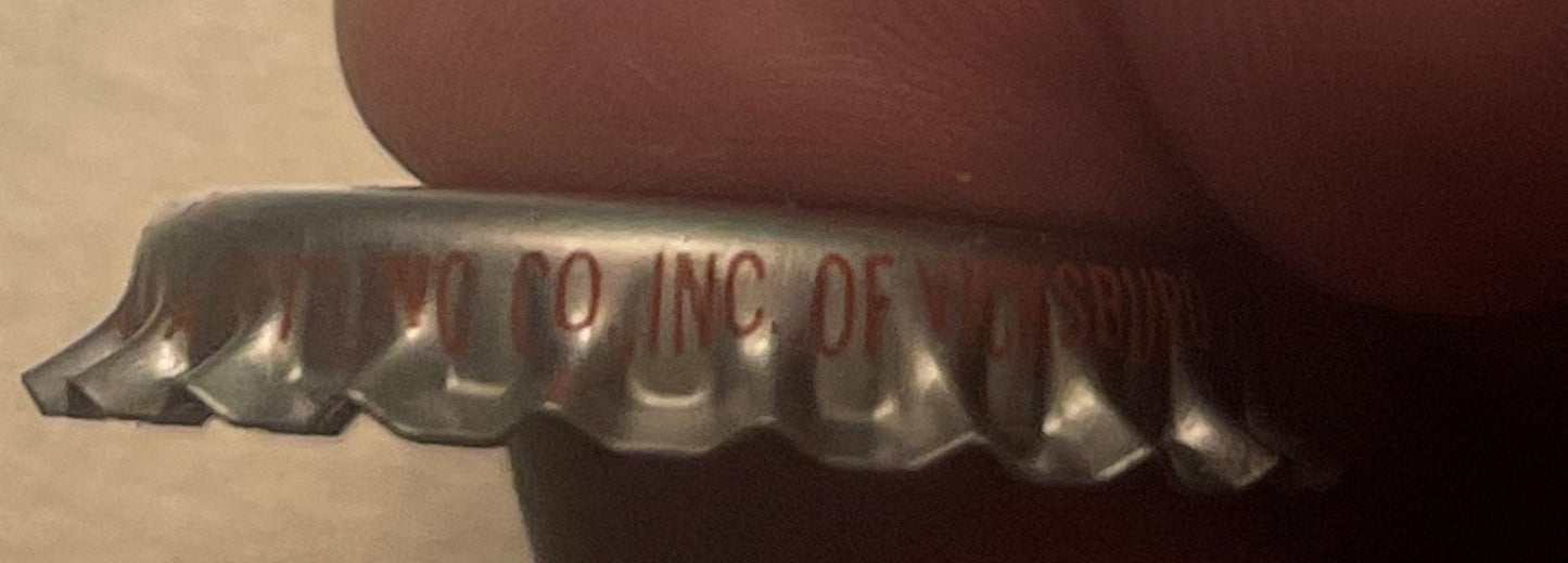 Close-up of a vintage Coca-Cola bottle cap showing embossed text and ridged metal edges against a brown fabric background.
