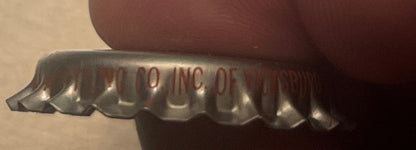 Close-up of a vintage Coca-Cola bottle cap showing embossed text and ridged metal edges against a brown fabric background.