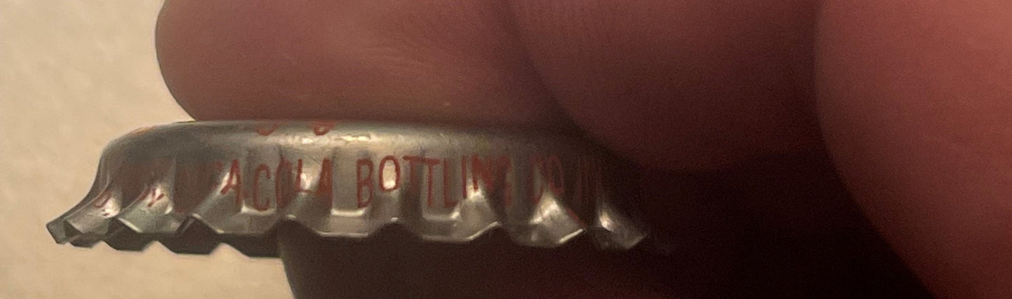 Close-up of a vintage metal bottle cap held by a thumb, showing embossed text including "BOTTL" and partial ingredients list 