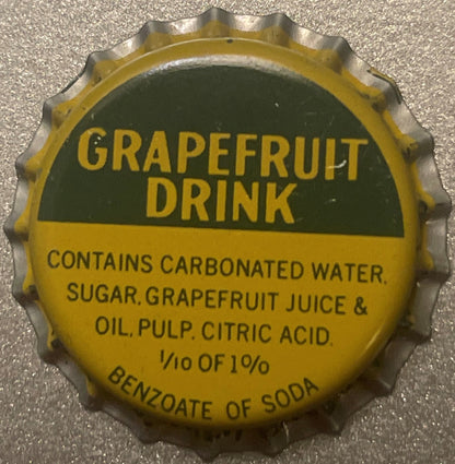 Vintage yellow and green grapefruit drink bottle cap with embossed crown edge and printed text on concrete surface.