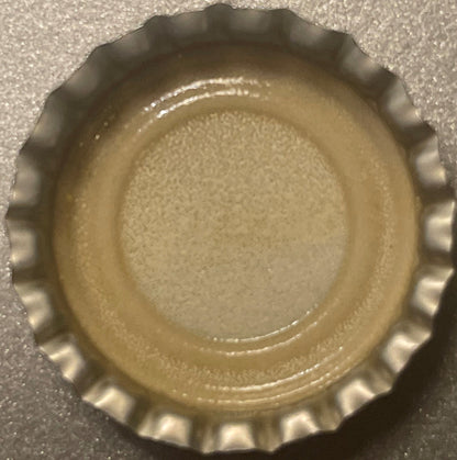 Vintage bottle cap with corrugated metal edge and cream-colored interior, photographed from above on textured surface