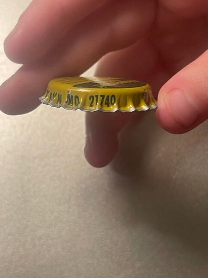 Vintage yellow bottle cap held in person's hand, showing embossed text and ridged metal edges against light background