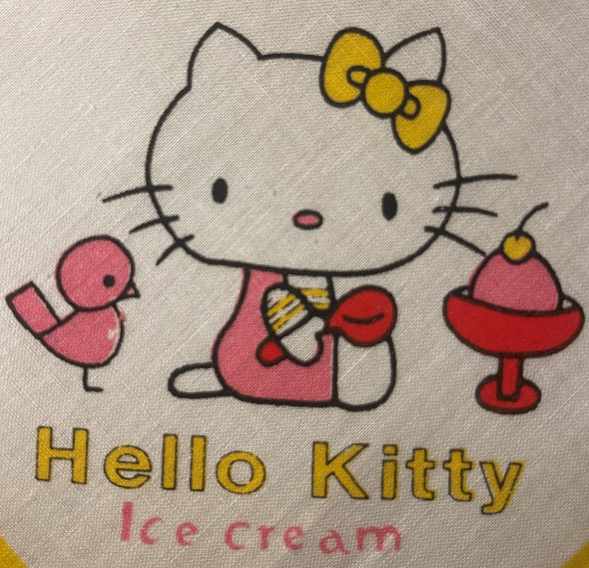 Vintage Hello Kitty cotton napkin with yellow bow and ice cream design printed on cream fabric, close-up flat lay view.