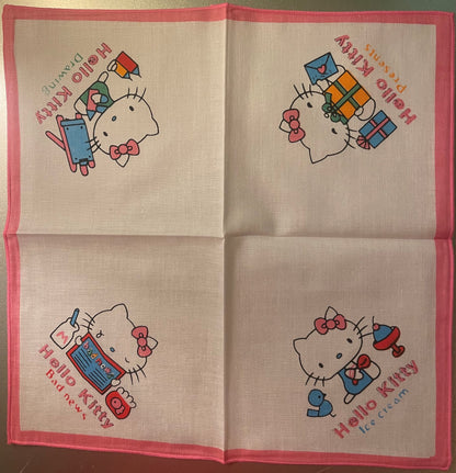 Unfolded pink-bordered cotton napkin displaying four Hello Kitty illustrations with colored text on cream fabric, laid flat o