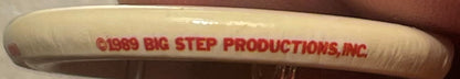 Close-up of vintage pin showing red text reading "©1989 BIG STEP PRODUCTIONS, INC" on cream-colored cylindrical surface