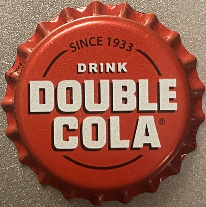 Red bottle cap with white text reading "DRINK DOUBLE COLA" and "SINCE 1933," shown flat against gray textured surface