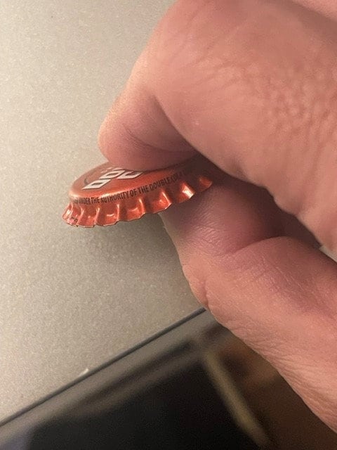 Red Double Cola bottle cap held between adult fingers showing corrugated ridges and partial text, close-up detail shot