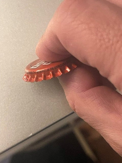 Red Double Cola bottle cap held between adult fingers showing corrugated ridges and partial text, close-up detail shot