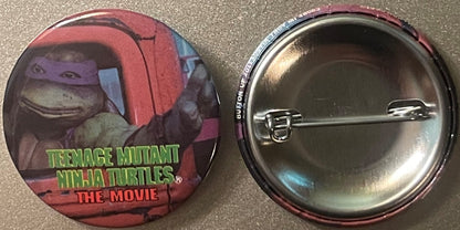 Front and back of a circular pinback button featuring a Teenage Mutant Ninja Turtles character in red mask with green text "T