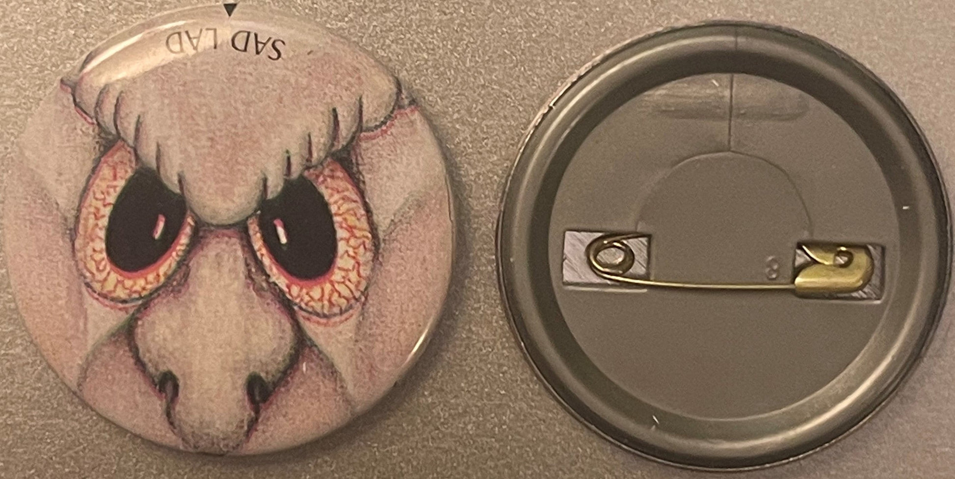 Vintage pin-back button showing front and back: front features illustrated sad creature with large bloodshot eyes and droopy 