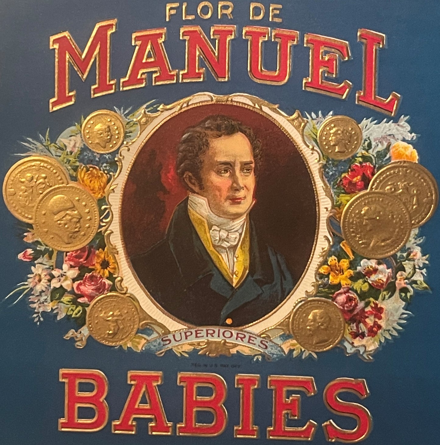Vintage cigar label with gold-embossed text "Flor De Manuel Babies," portrait of a man in formal dress surrounded by gold coi