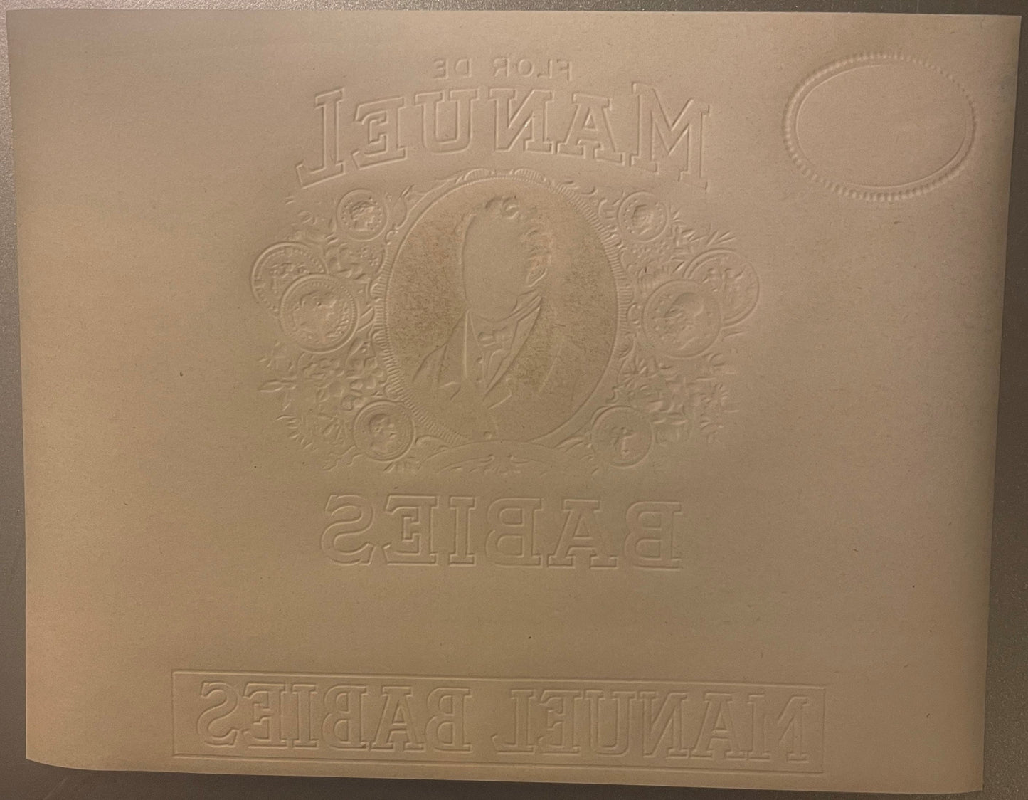 Cream-colored embossed cigar label featuring a portrait medallion surrounded by decorative circular motifs, with "Manuel" at 
