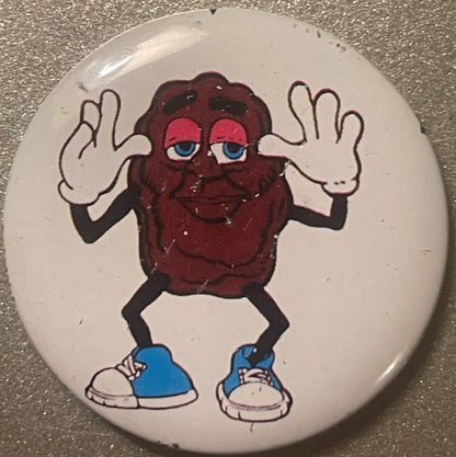 Vintage tin pin featuring a brown raisin character with blue eyes and shoes, white gloves raised in jazz hands pose against c