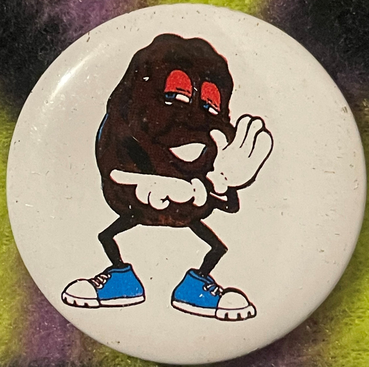 Vintage California Raisin tin pin featuring a cartoon character with dark body, red sunglasses, white gloved hands, and blue 
