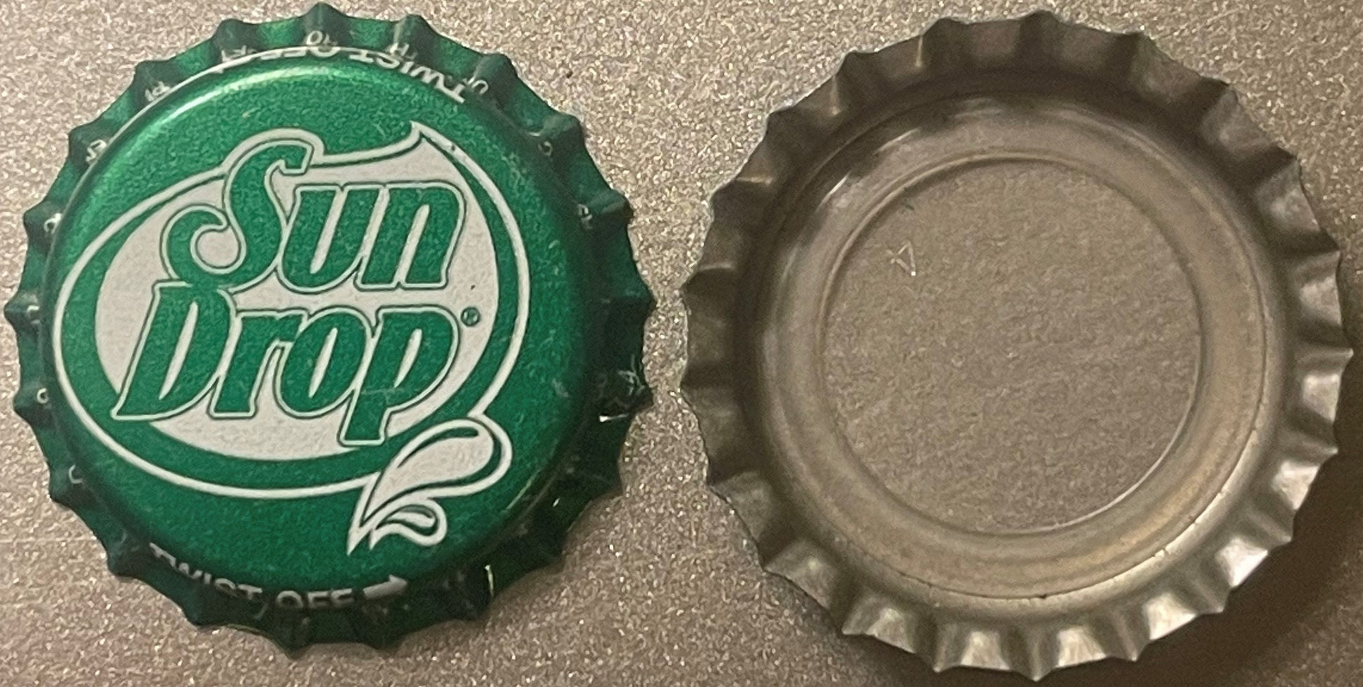 Front and back of a green Sun Drop bottle cap with cream-colored script logo and twist-off crown ridges visible against gray 