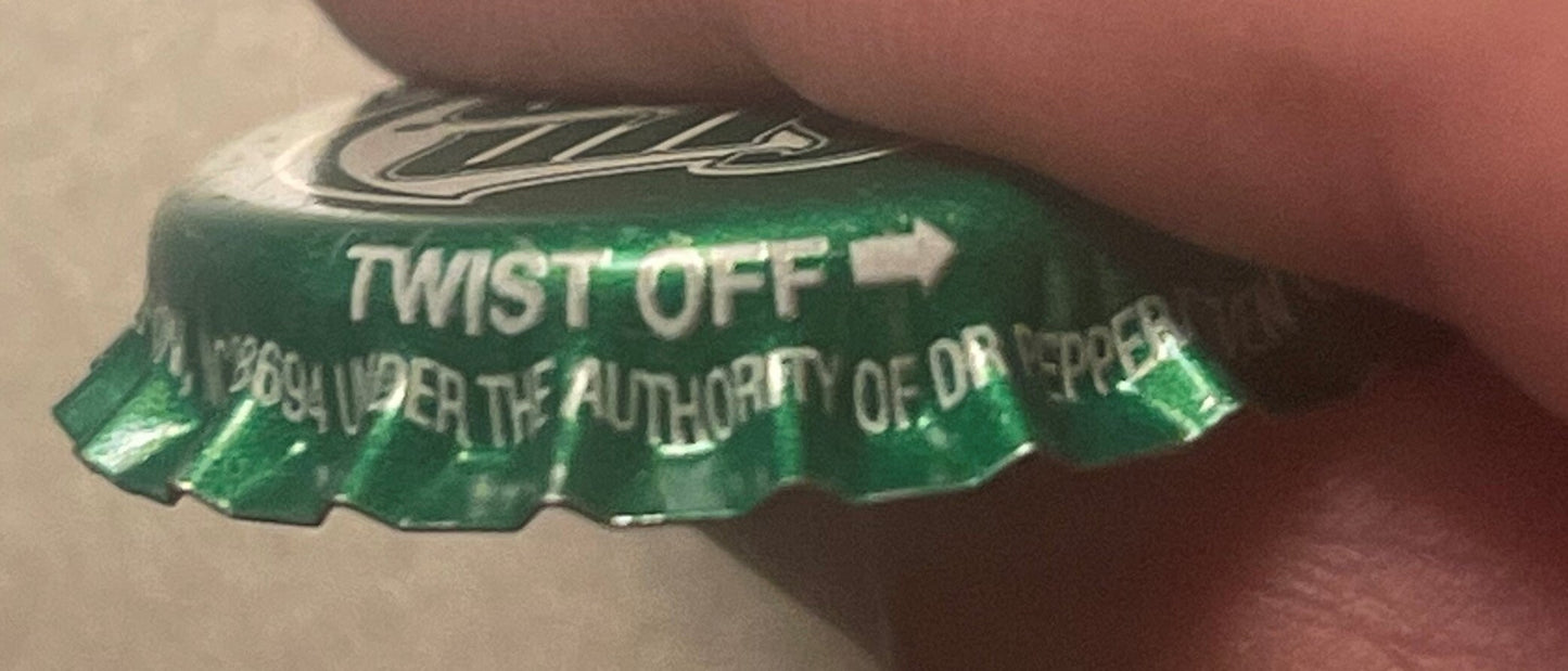 Close-up of green twist-off bottle cap held by a finger, showing "TWIST OFF" text and partial lettering about authority, with