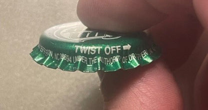 Green twist-off bottle cap held by a finger for scale, showing "Sun Drop" branding and West Jefferson NC text embossed on whi