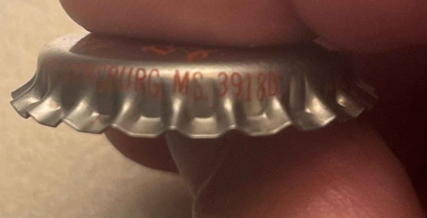Close-up of a silver metal bottle cap with ridged edges and red embossed text listing ingredients, photographed at an angle a