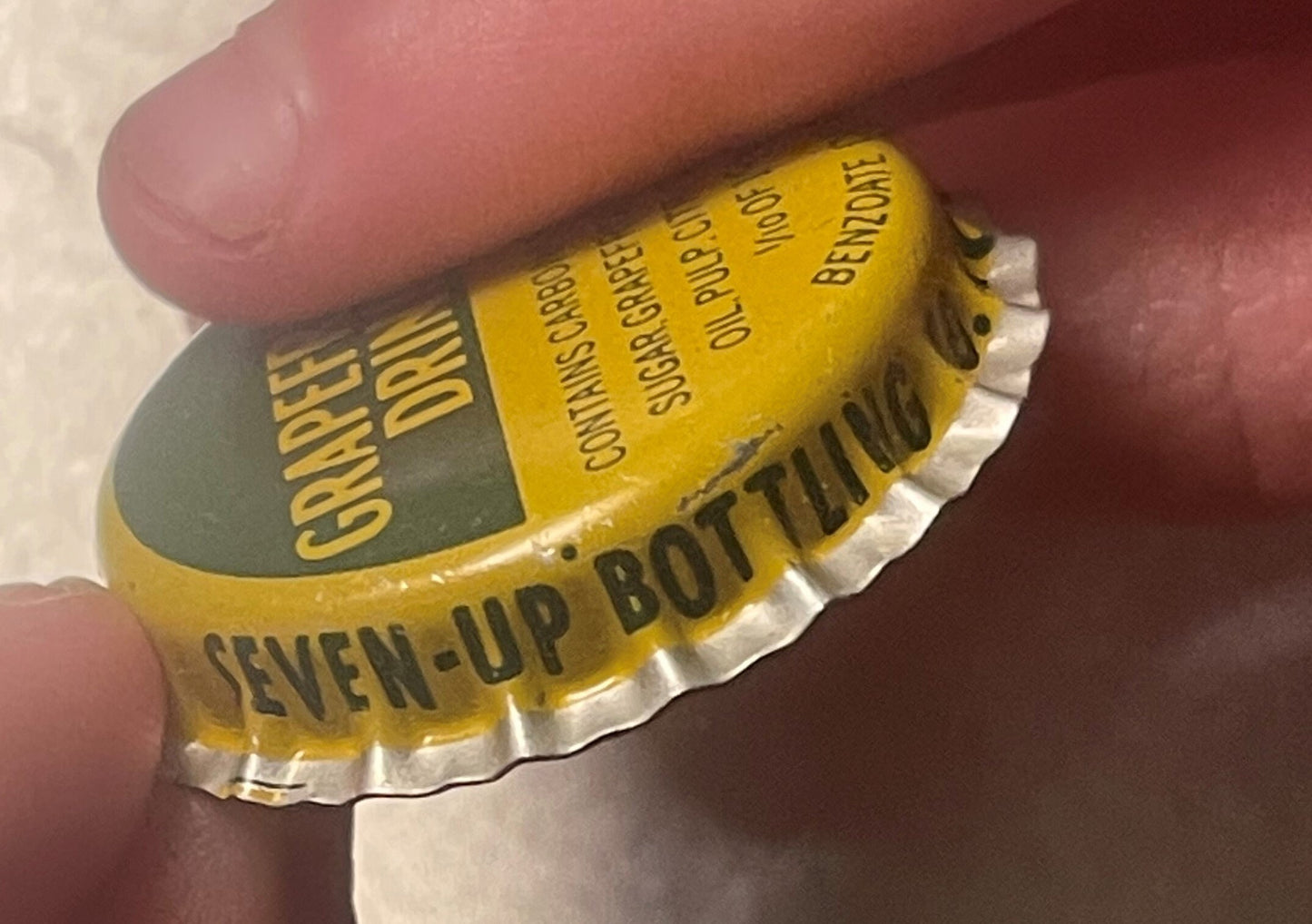 Vintage yellow bottle cap with white ridged edge held in fingers, showing "Seven-Up Bottling" text and Hagerstown MD origin d