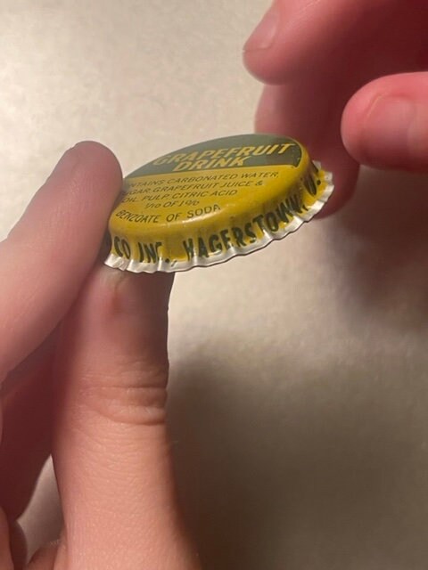 Yellow vintage bottle cap held in hand, printed with "Seven-Up" and "Hagerstown MD" text, shown at close angle for detail
