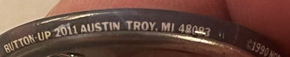 Close-up of pin back showing embossed text "BUTTON-UP 2011 AUSTIN TROY, MI 48027" on dark metal surface