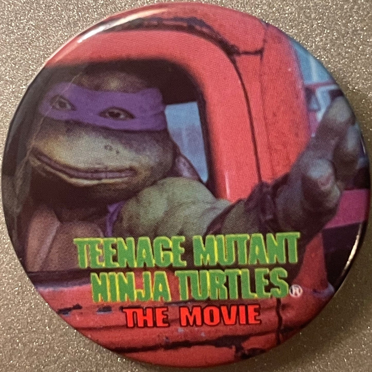 Circular red pinback button featuring purple-masked turtle character with "TEENAGE MUTANT NINJA TURTLES THE MOVIE" text in gr