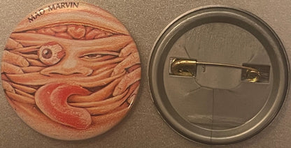 Front and back of a terracotta pinback button featuring embossed grotesque face with bulging eyes and text reading "MAD MARVI