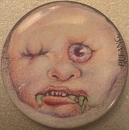Vintage 1980s Pufang pinback button: a pale bald baby head with one eye shut, one bulging pink-rimmed eye, little fangs and green drool, PUFANG on the right edge