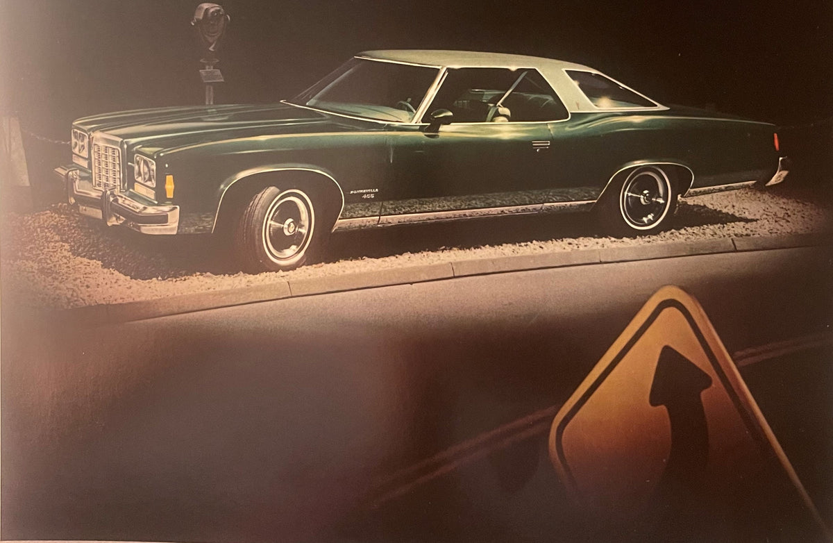 Vintage 1974 Pontiac Bonneville dealer brochure page showing dark green hardtop coupe photographed at night against gravel, with trophy visible on hood; orange triangle logo in foreground.