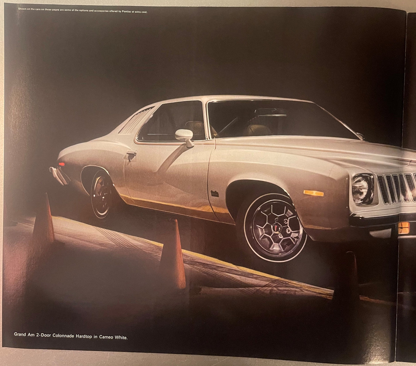 Cream-colored Pontiac Grand Am 2-door Colonnade Hardtop displayed against dark background with orange safety barriers visible