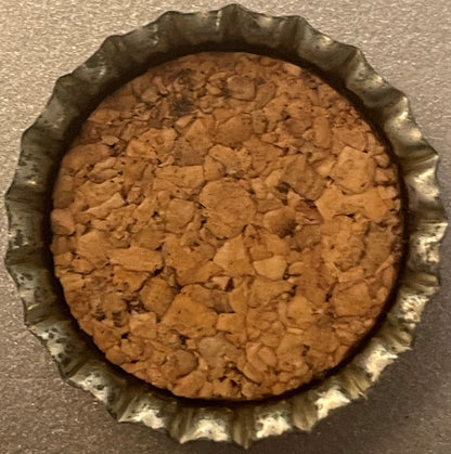 Inside of a cork-lined bottle cap seen from above, showing the cork disc inside a crimped metal rim.