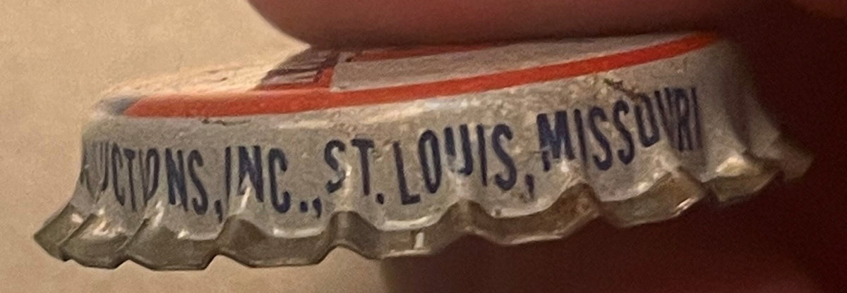 Close-up of vintage cork-lined bottle cap with "...PRODUCTIONS, INC., ST. LOUIS, MISSOURI" text, red stripe and decorative scalloped edge