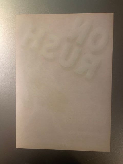 Cream-colored vintage vegetable crate label with embossed text, photographed flat against gray wall showing faint lettering a