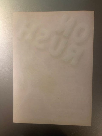 Cream-colored vintage vegetable crate label with embossed text, photographed flat against gray wall showing faint lettering a
